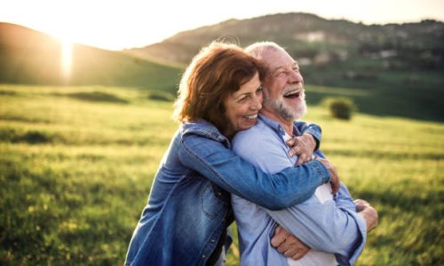Happy senior couple outside in spring nature, hugging at sunset. Side view.