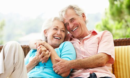 Senior Couple Sitting On Outdoor Seat Together Laughing